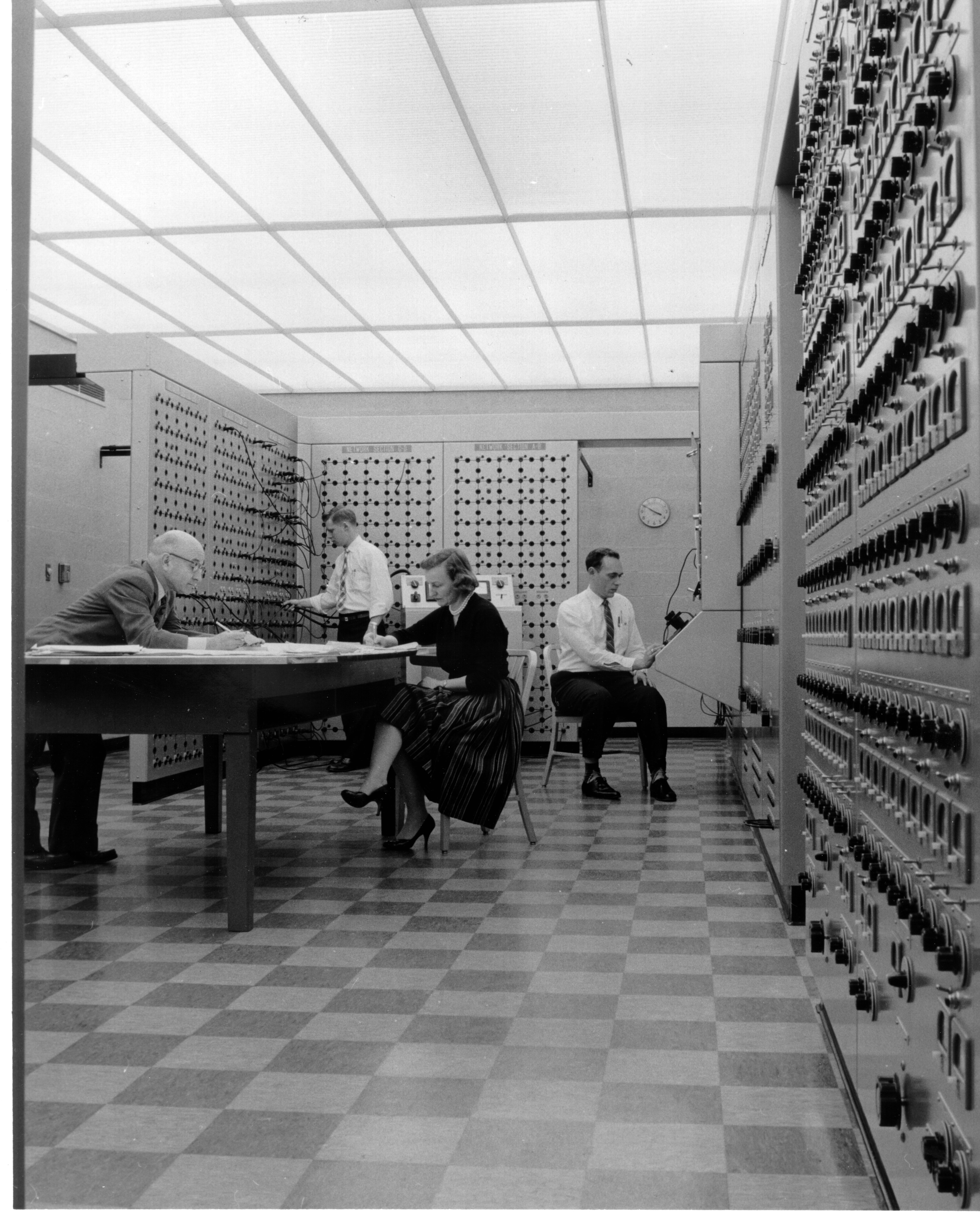 Black and white photo of four people working with an analog computer.